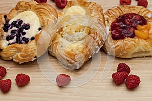 Assortment of cheese danishes puff pastry with blackberries, vanilla custard, cherry jam and fresh raspberries on wooden backgroun