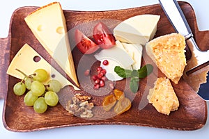 Assortment of cheese with fruits, grapes, nuts and cheese knife on a wooden serving tray.