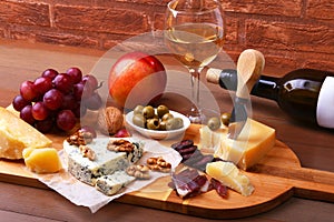 Assortment of cheese with fruits, grapes, nuts and cheese knife on a wooden serving tray.