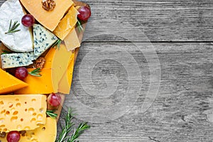 Assortment cheeses on wooden cutting board. Cheese plate served with grape fruits, tomatoes and rosemary, various cheese