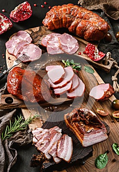 Assortment of cold meats products, ham, sausage, salami, parma, prosciutto, bacon on wooden cutting board with herb and spices