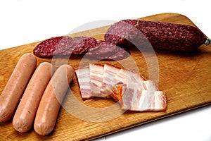 Assortment of delicious deli meats on wooden board, isolated on white