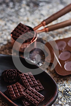 Assortment of different chocolate types in wooden carved plate, with vintage props on the background