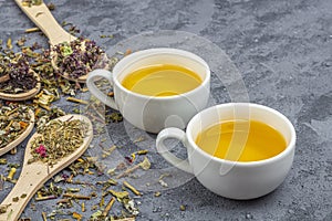 Assortment of different grade dry tealeaf in wooden spoons and two cup of green tea. Organic herbal, green and black tea with dry photo