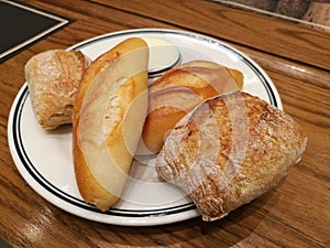 Assortment of different types of French bread as side dish serve with salted butter on table, focus-on-foreground bread with blur