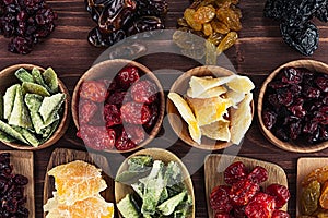 Assortment of dried fruits in spoons, bowls on brown wooden background.