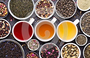 Assortment of dried tea leaves, fruit and herbs in bowls  and cups of tea