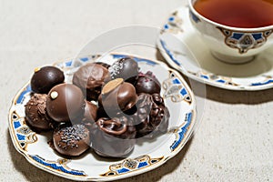 Assortment of fine filled chocolate bonbons on a plate with a cup of red tea
