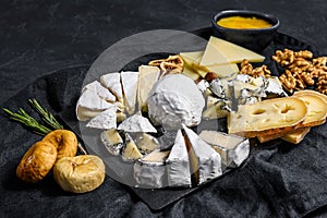 Assortment of French cheese with honey, nuts  and figs on cutting board. Italian antipasto. Black background. Top view