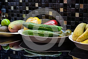 Assortment of fresh fruits and vegetables on the kitchen table against the background of dark small tiles on the wall