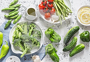 Assortment of fresh garden vegetables - asparagus, broccoli, beans, peppers, tomatoes, cucumbers, garlic, green peas on a light ba