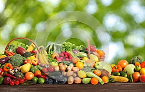 Assortment of fresh organic vegetables and fruits on wooden table against blurred green background