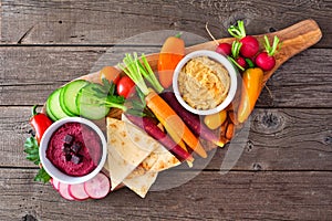 Assortment of fresh vegetables and hummus dip on a serving board, top view on rustic wood