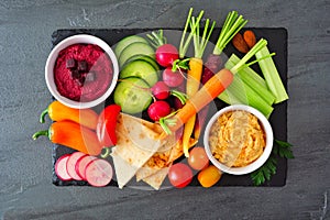 Assortment of fresh vegetables and hummus dip on a serving platter, above view on slate