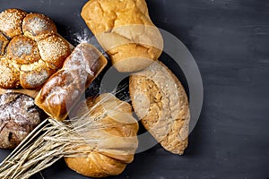 Assortment of freshly baked breads with ears of wheat on black background. Shallow depth of field