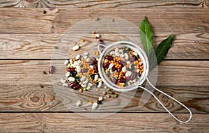 Assortment of legumes in a stainless drainer and spilled on a wooden tabletop background, top view.