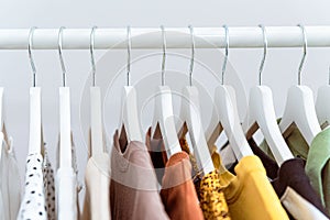 Assortment of many cotton clothes hanging in row on white coat hangers.