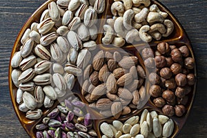 Assortment of nuts in ceramic bowl on a wooden background, close up, top view, copy space. Cashew, hazelnuts, pistachios and