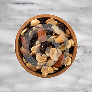 Assortment of nuts and dried fruit in a wood bowl atop a gray marble countertop top view