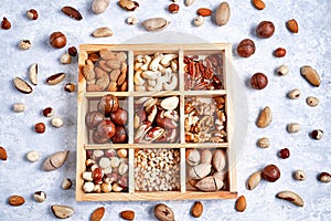 Assortment of nuts in a wooden box, on a blue background. pecans, hazelnuts, almonds, pine nuts, brazil nut, cashews