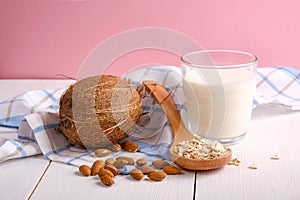 Assortment of organic vegan non dairy milk from nuts in glass on a wooden table on pink background. Coconut, almond nuts, spoon of