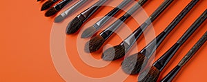 Assortment of Professional Makeup Brushes on a Vibrant Orange Background, Beauty Tools Concept