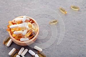 Assortment scattered pharmaceutical medicine tablets, pills, drugs in wooden bowl on gray background. White food dietary