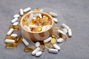 Assortment scattered pharmaceutical medicine vitamins, pills, drugs in wooden bowl on gray background. White food