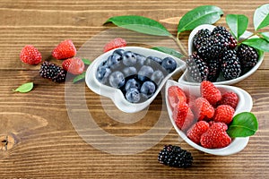 Assortment of seasonal fruits, berries in the white bowls on the wooden background