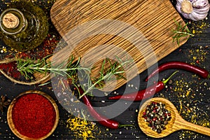 An assortment of spices on a black background, a cutting board and rosemary branches