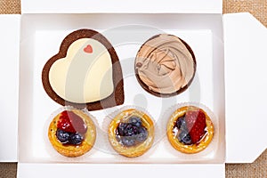 Assortment of sweet cakes, strawberry and blueberry fruit tarts, heart cake on white paper box