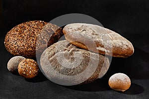 Assortment of tasty baked round bread and buns with sesame and sunflower seeds, sprinkled with flour. Black background