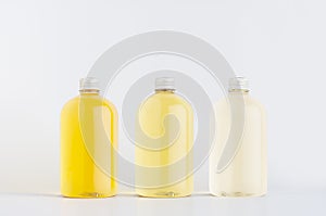 Assortment of three plastic low thick bottles with pale fresh drink different yellow colors or cosmetic essential oil, silver cap.