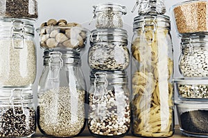 Assortment of uncooked grains, cereals and pasta in glass jars on wooden table. Healthy cooking, clean eating, zero