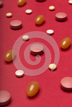 Assortment of various colourful pills red coloured background. Medication and prescription pills.