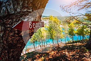 Assos village Kefalonia. Greece. Beach wooden arrow sign on a pine tree showing direction to small hidden beach