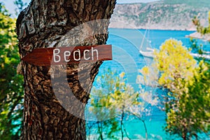 Assos village, Kefalonia. Greece. Beach wooden arrow sign on a pine tree showing direction to small hidden beach. White