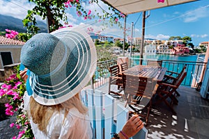 Assos village, Kefalonia, Greece. Female tourist in blue sunhat in front of cozy veranda terrace door admiring turquoise