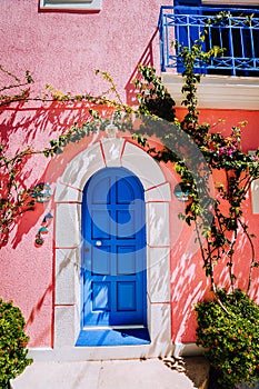Assos village. Traditional lilac colored greek house with bright blue door and fucsie plant flowers around. Kefalonia