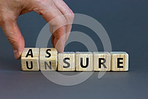 Assure or unsure symbol. Businessman turns wooden cubes and changes the concept word unsure to assure. Beautiful grey table, grey photo