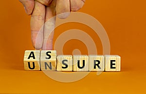 Assure or unsure symbol. Businessman turns wooden cubes and changes the concept word unsure to assure. Beautiful orange table, photo