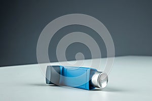 An asthma inhaler lies on a white table against a gray background, an asthmatic attack. The concept of treatment of bronchial
