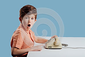 Astonished boy pointing at old telephone on blue background