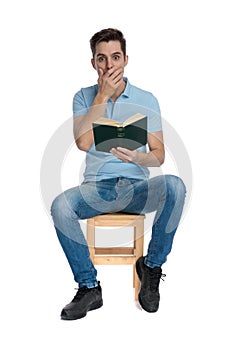 Astonished casual man covering his mouth and holding a book
