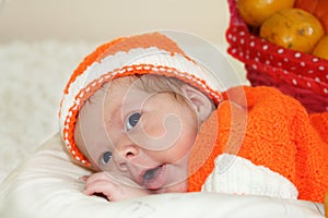 Astonished cute newborn baby dressed in a knitted orange costume