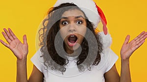 Astonished girl in Santa hat saying Wow, pleasantly surprised by New Year gifts