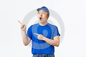 Astonished and impressed asian delivery guy in blue cap and t-shirt drop jaw surprised and astounded while pointing and