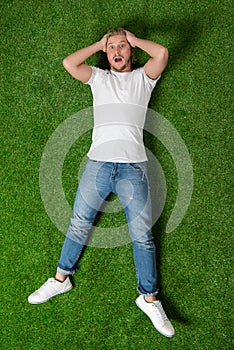 Astonished man with hands on head lying on the meadow