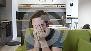 Astonished man scared by the news looks at the camera on couch in living room. Portrait of shocked and surprised man