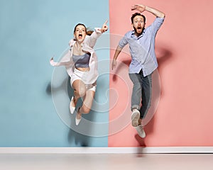 Astonished man and woman running, jumping isolated over blue and pink background. Human emotions, youth, love and active